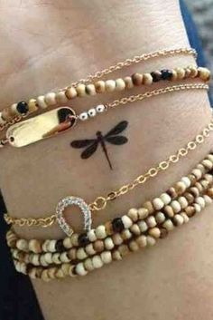 three bracelets with different types of beads and charms on the wrist, one has a dragonfly