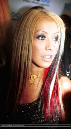 a woman with red and black hair is looking at the camera while wearing gold jewelry