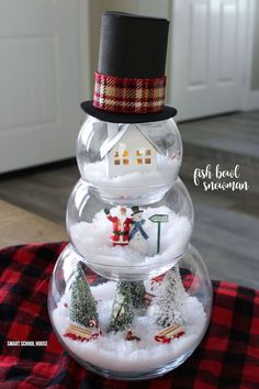 a snowman is sitting on top of a glass bowl filled with snow and trees