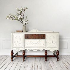 an old dresser with flowers on top is in the corner of a white painted room