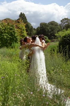 two women in wedding dresses are walking through tall grass