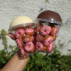 two plastic containers filled with pink frosted donuts in front of a white wall