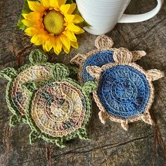 three crocheted turtle coasters next to a coffee cup and sunflower on a table