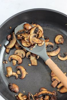 mushrooms being cooked in a skillet with a wooden spatula on the side,