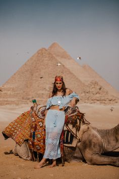 a woman sitting on top of a camel near the pyramids