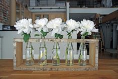 four vases with white flowers in them on a wooden shelf near a brick wall