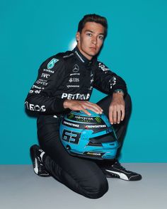 a man sitting on the ground wearing a racing suit and holding a helmet in his hands