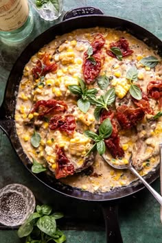 a skillet filled with corn, tomatoes and green leaves on top of a table