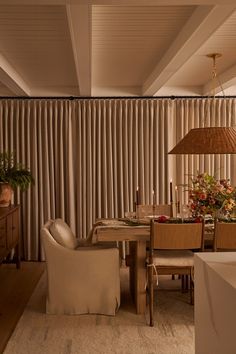 a dining room table and chairs in front of a curtained window with vertical blinds