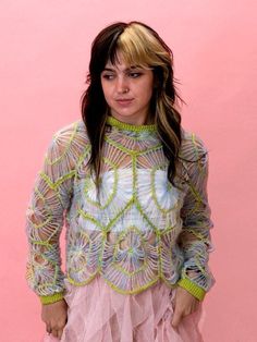 a woman with long hair wearing a colorful sweater and tutu skirt standing in front of a pink wall