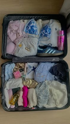 two open suitcases filled with clothes on top of a wooden floor