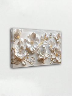 a white and gold wall hanging with flowers on it's side, in the middle of a room