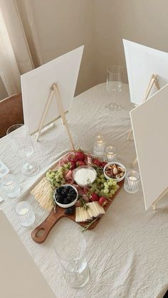 a table topped with cheese and fruit on top of a wooden cutting board next to two easers