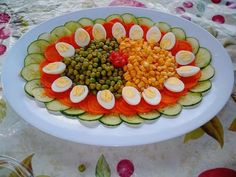 a platter filled with sliced vegetables and hard boiled eggs on top of cucumbers