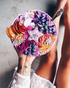 a woman's legs holding a plate with fruit and flowers on it while sitting down