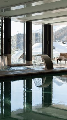 an indoor swimming pool surrounded by large windows and snow covered mountains in the background,