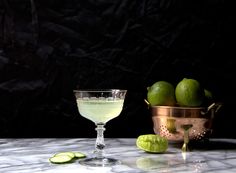 a glass filled with liquid next to limes and a bowl full of limes