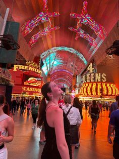 a woman standing in the middle of a mall looking up at neon signs on the ceiling