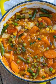 a yellow pot filled with vegetable soup on top of a wooden table next to a white napkin