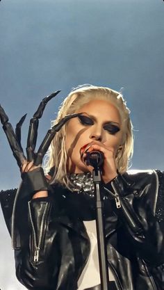 lady in black and white outfit holding up her hands to the side while singing into a microphone