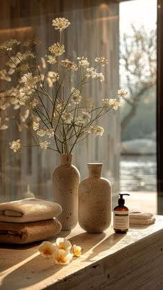 two vases with flowers in them sitting on a window sill next to towels