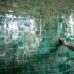 a man painting a wall with green tiles