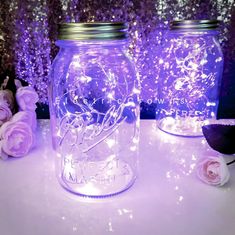 two mason jars with fairy lights in them sitting on a table next to some flowers