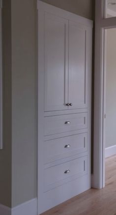 an empty room with white cabinets and wood flooring in front of a door that leads to another room