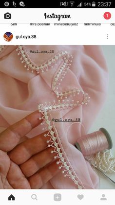 the thread is being sewn on to a pink shirt with pearls and beads hanging from it