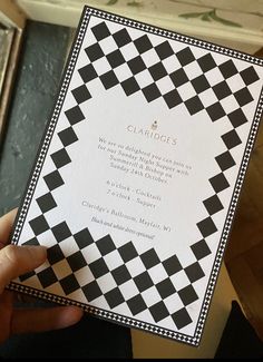 a person holding up a black and white checkerboard wedding card in their hand