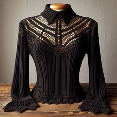 a black sweater with crocheted details on the shoulders and neck, sitting on top of a wooden table