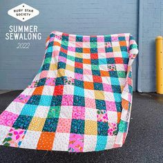 a colorful quilt sitting on the ground next to a yellow pole and blue brick wall