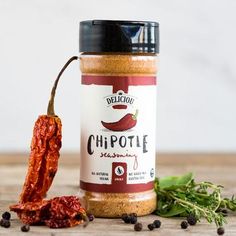 a jar of chipotle seasoning next to some chili peppers on a wooden table