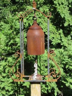 an old fashioned bell hanging from a metal stand in front of some green bushes and trees