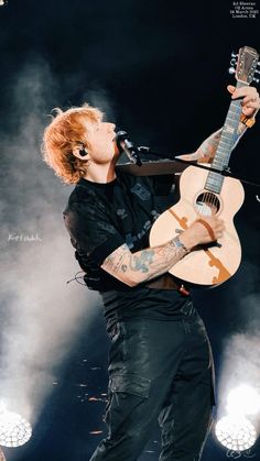 a man with red hair holding a guitar in his right hand and singing into the microphone