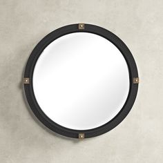 a round mirror mounted on the wall with metal studs and wood trim around it