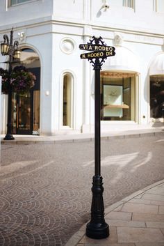 a street sign on a pole in front of a white building with windows and shops