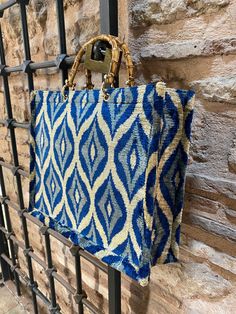 a blue and white handbag hanging on a black iron fence next to a stone wall