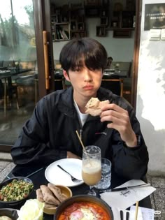 a man sitting at a table with food in front of him and eating something out of his hand