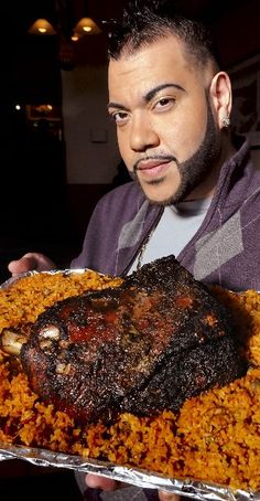 a man holding up a large piece of meat covered in rice