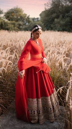 a woman in a long red dress standing in a field with her hands on her hips