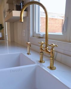 a kitchen sink with two brass faucets in front of a white counter top