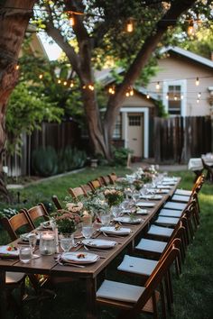 A long outdoor dining table set with place settings, flowers, and candles under string lights in a lush backyard with trees and a small house. Large Backyard Party, Small Backyard Dinner Party Ideas, 50th Birthday Backyard Party Ideas, Small Celebration Ideas, Fun Backyard Party Ideas, Casual Backyard Party, Small Backyard Party, Backyard Dinner Party Table, Event Venue Business