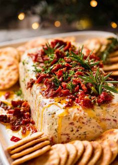 a platter with crackers, cheese and sauce on it next to a christmas tree