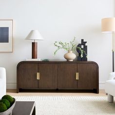 a living room with white furniture and green plants on the sideboard in front of it