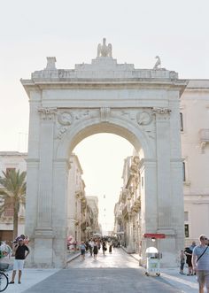 people are walking down the street in front of an arch