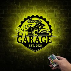 a hand holding a remote control in front of a brick wall with the garage logo on it