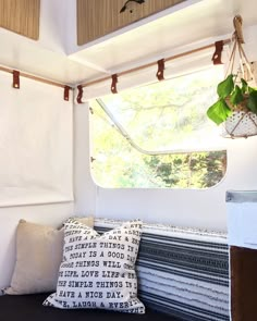 a couch with some pillows on it and a window in the back ground, behind which is a potted plant