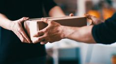 two people are holding a box in one hand and the other is handing it to another person