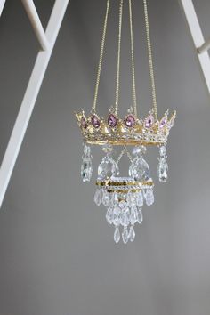 a tiara hanging from a white ladder with crystal beads and gold chains on it